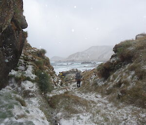 The boys in the distance walking though snow covered hills it’s snowing the ocean is in the distance