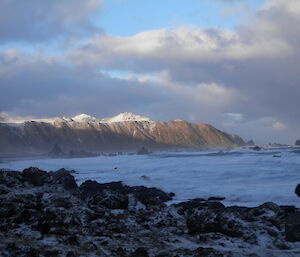 View across the bay at Double Point. There is snow on the ground and the distant white snow covered peaks above the coast are lit up by the sun