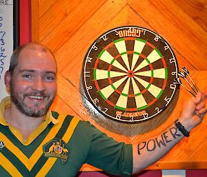 Craig, standing in front of the dart board. He is holding his three darts and has ‘POWER’ written on his arm.