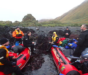 The boat crew with their wet suites on sitting down on the boats eating lunch