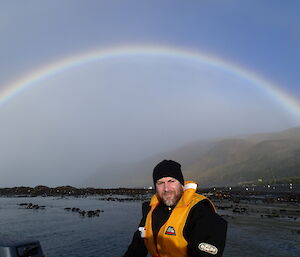 Mark in a his dry suit sitting with the water behind him and a rainbow in the background