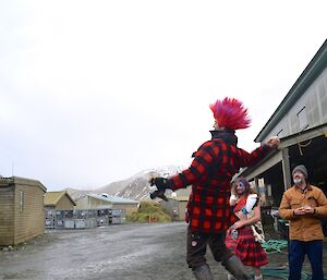 Steve, standing on a half drum and wearing a pink and red mohawk wig, in the motion of throwing a haggis