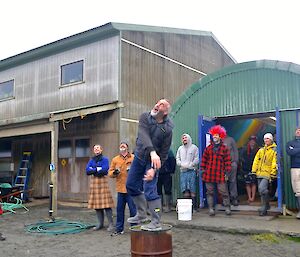 Greg, standing on the half drum, having just hurled his haggis, while behind him a group of several onlookers follow its flight