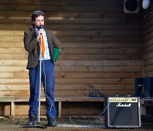 Race caller Dean standing on the mess porch, calling (into a microphone) the field in the "mounting Yard"