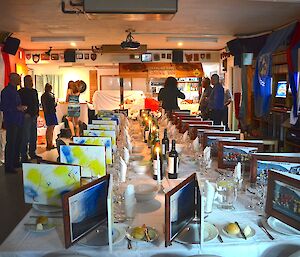 The fabulous set up for miidwinter dinner. The menus were framed pictures joined with brass hinges — a great memento. There are several well dressed expeditioners admiring the set up. The walls are adorned with flags of all the nations that are part of the Antarctic Treaty