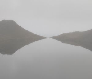 Waterfall Lake seen through fog in calm winds, showing a perfect reflection of the hills on the opposite shore