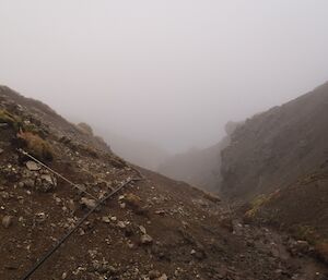 View from the dam down Gadgets Gully shrouded in mist. The black poly water pipe can be seen on the left (southern) slope of the gully