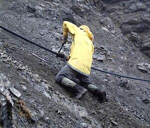 Josh on the scree slope on his knees just below the pipe he is repairing