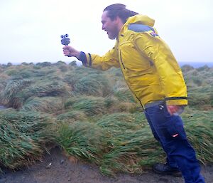 Aaron leaning into the wind alongside Razorback Ridge. He is holding a hand held anemometer and is at an angle of about 30 degrees to the vertical