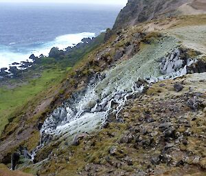 A running waterfall with frozen icicles and ice crystal in the foreground looking down into Sellick Bay with the west coast surf in the background