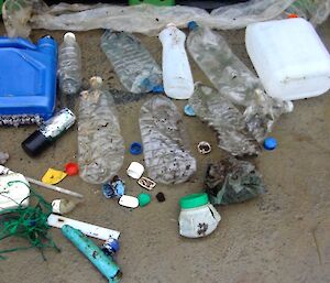 A collection of marine debris spread out on the ground. It includes plastic bottles, various pieces of hard and soft plastic and some lengths of green fishing twine. It was found on the walk back from Bauer Bay to the station