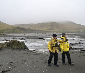 Bauer Bay marine debris clean up: Chris showing Clive the area we are to work in. They are standing on a wide expanse of the beach with the distant hills in the background shrouded in mist and cloud
