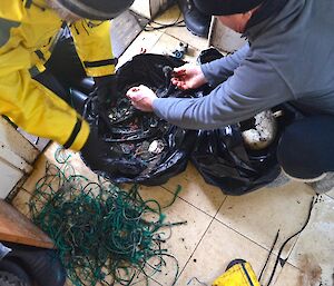 Clive and Chris in the small cold porch of Bauer Bay hut, sorting through the bag of marine debris, for ease of collating and counting. The green fishing twine has been separated and is in a small pile beside the bag