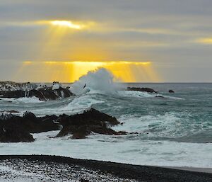 Green Gorge Light — looking over the ocean at crepuscular rays poking through the cloud while the surf breaks over the rocks in the centre foreground with a silhouette of a bird on the spray