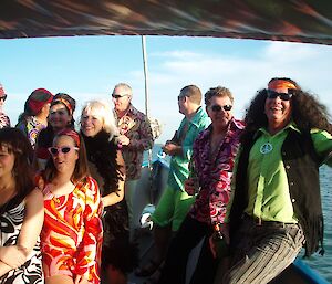 Dave in his hippy phase. Dave with several friends on a boat. Dave is dressed in a lime green shirt, frilled waist coat, has a ‘peace’ symbol pendant and has long frizzy hair tied with a orange head band