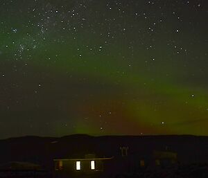 View of a weak aurora australis, coloured in shades of green and red, against a star encrusted clear sky