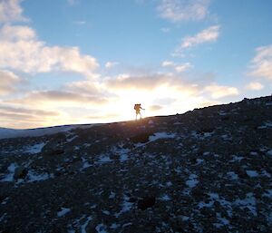 Tom silhouetted against the sun walking up a slope near Bauer Bay