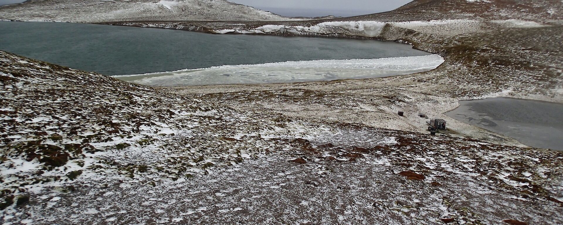 Frozen lakes near Windy Ridge — taken from a high vantage points shows a snow covered landscape with some hills in the background a partially frozen lake on the left and a smaller lake on the right. Windy Ridge hut is near the shore of the smaller lake
