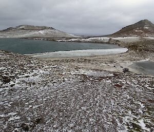Frozen lakes near Windy Ridge — taken from a high vantage points shows a snow covered landscape with some hills in the background a partially frozen lake on the left and a smaller lake on the right. Windy Ridge hut is near the shore of the smaller lake