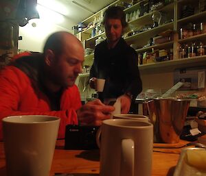 Mark and Tom in Hurd Point hut. in the back you can see four shelves along the length of the wall, fully stocked with food supplies