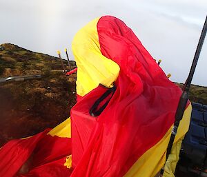 Mark fully wrapped in a red and yellow bivvy on Mt Waite