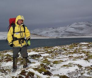 Josh, in all his cold weather gear and carrying his survival pack, standing on the snow covered track. Behind him is a lake and snow covered hills beyond