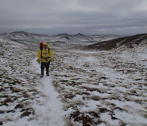 Josh walking along the track which is covered in snow. Behind him are snow covered hills