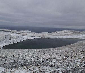 A snow covered scene, taken from the track. The small Endeavour Lake is down the gentle slope and the ocean can be seen beyond