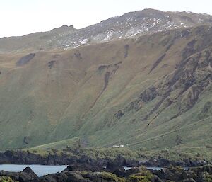 The steep slope of the Hurd Point jump up seen for somewhere on Hurd Point. Hurd Point hut can be seen dwarfed at the base of the slope. There is some snow still visible on the hills above the jump up slope