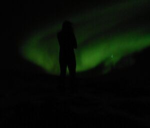 Ange silhouetted in front of the green aurora australis at Windy Ridge