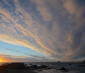 Sunset over Hasselborough Bay, giving an orange tinge to the underside of middle level bands of cloud. North head is silhouetted on the far bottom right of the picture