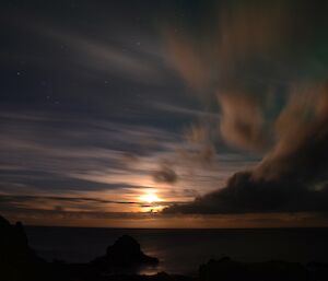 Full moon partially visible through scattered cloud, with the green tinge of an aurora in the right of picture