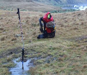 View of the pathway with a pack and two walking poles, one pole has only the handle showing with about one meter of it is lost in what looks like a small puddle but is in fact a deep water trap for the unwary