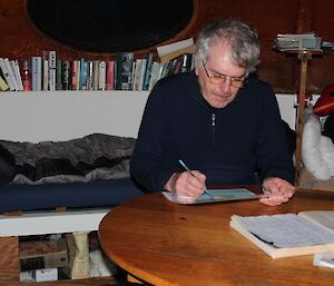 Tony sitting at a table in Waterfall Bay hut, studying a map of the area, planning the walk for the next day