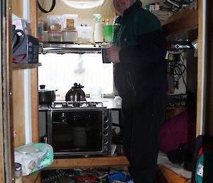 Nick standing inside Windy Ridge shelter with a cup of tea. The hut is a very small field accommodation shelter