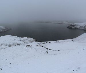 A small lake on the plateau, surrounded by snow and mist or low cloud