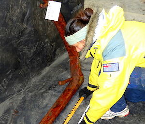 More cataloguing . Patty kneels down in front of a large piece of rusted steel. She is using a tape measure. Each item was rephotographed, records updated before being placed back in storage. Some of the catalogues and records date back to work done previously in the mid 1970’s.