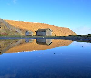 Late morning view of the magnetic quiet zone reflected in a small pond. The huts, the orange, green and brown shades of the escarpment and the azure clear sky almost perfectly reflected in the pond