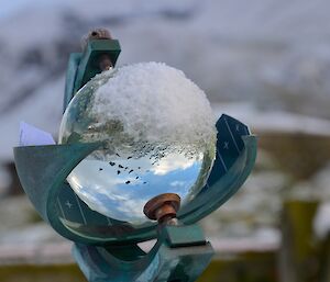The crystal ball at Met — the glass (crystal) ball is mounted in a brass fitting and is used to measure hours of sunshine. There is an inverted image of the sky and escarpment in the ball and some snow stuck to the top