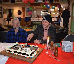 Barry cutting the large chocolate mud cake with a big knife. Another expeditioner (Lionel) looks on,