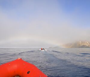 Heading for the pot of gold — The red bow of a IRB is in the immediate left foreground with another IRB up ahead heading towards a fog/rainbow. The slopes of the escarpment, shrouded in low cloud and mist, are in the distant right background