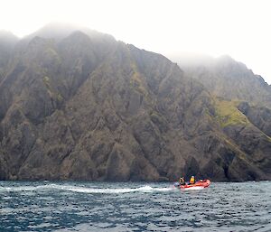 One of the boats motors along below the steep jagged rocky slopes that rise up directly out of the ocean on the southern coast of Macquarie island