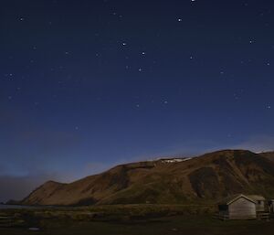 Night scene illuminated by the full moon. Many stars show up in the sky while the snow capped escarpment is visible under the light of the full moon