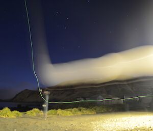 Time exposure of weather balloon launch at night — shows the balloon as a lighter band as it is brought out of the balloon shed then the band heads skyward after release. A thin green line (battery light) parallels the balloon streak