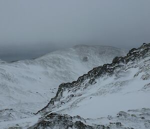 Looking east from the ABC track across a snow covered landscape, consisting of ridges and valleys with the ocean visible in the distance