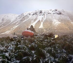 View of Waterfall Bay hut (red ovoid) from just to the east across the tussock with the escarpment in the background. The whole scene is covered in snow