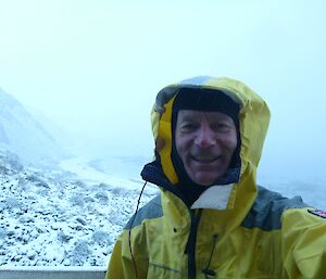 Picture of John (top half) wearing his yellow wet weather gear and a snow covered landscape in the background