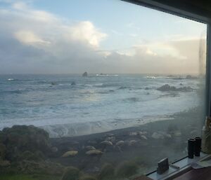 Hurd Point Channel — Looking through a hut window onto the coast of Hurd Point with an Ele seal harem on the waters edge, some surf and clouds in the background