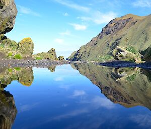 Rare calm day at Hurd Point. Taken from amongst the rock stacks showing a perfect reflection in a small pond of the escarpment the cirrus streked sky and some small tussock covered rock stacks