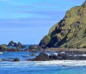 View to the west of Hurd Point hut showing the steep rugged escarpment and the rock stacks just offshore, with one of the stacks in the shape of a pointed arch. At the very end of the beach is a elephant seal harem